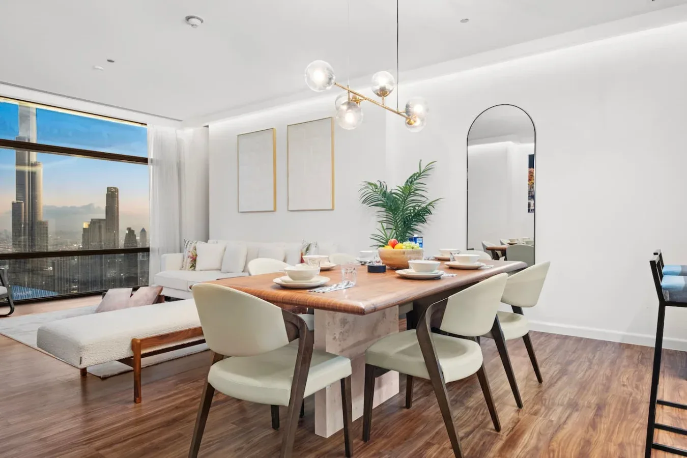 A bright dining area with a wooden table, light seating, and large windows.