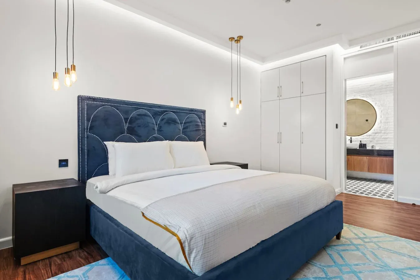 A bedroom with a large bed, dark blue upholstered headboard, and white bedding.