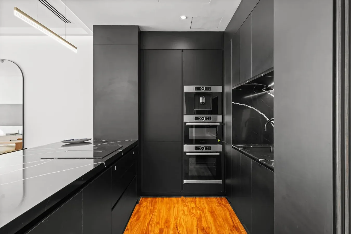 A modern kitchen with dark cabinetry, built-in appliances, and a wood floor.