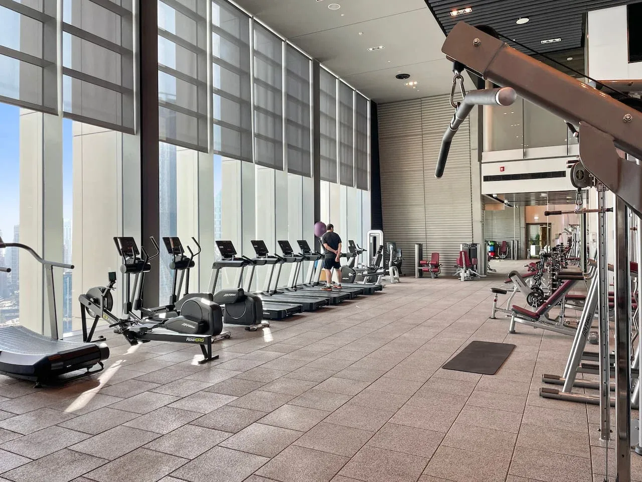 A spacious gym with exercise machines beside tall windows.