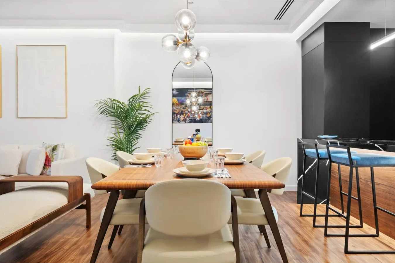 A dining area with a long wooden table, light seating, and pendant lights.