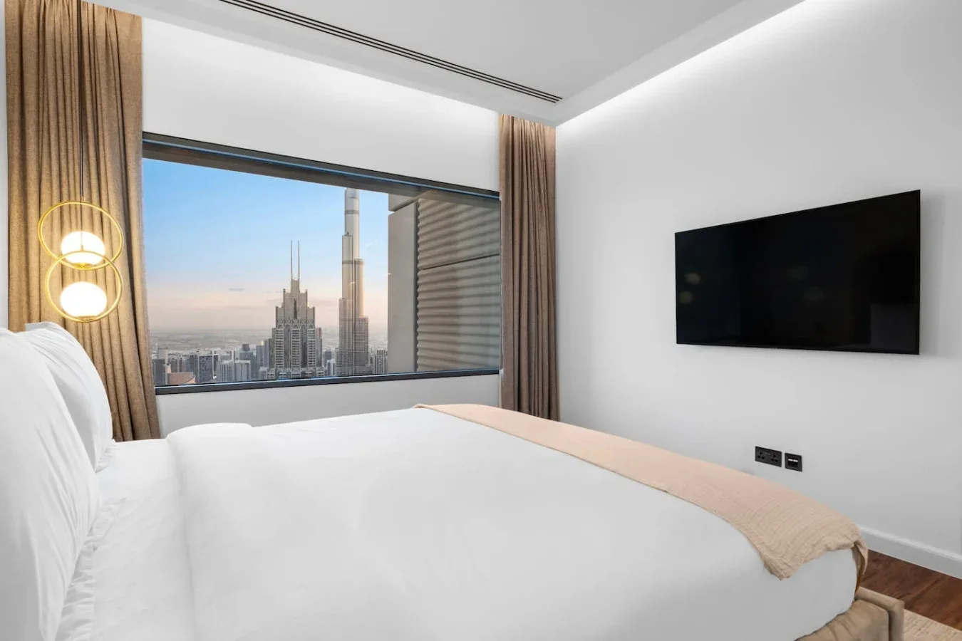 A bright bedroom has a large window overlooking a city skyline.