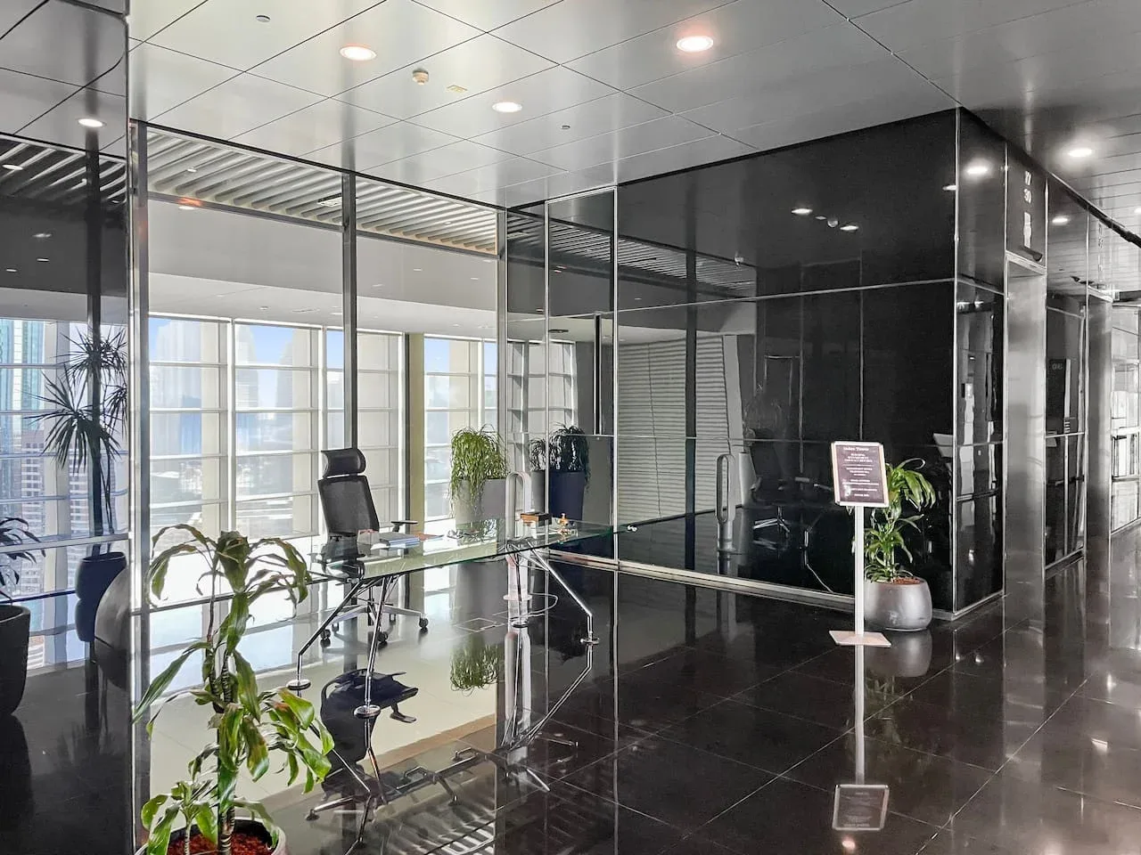 A modern office reception area with glass walls, a desk, and indoor plants.