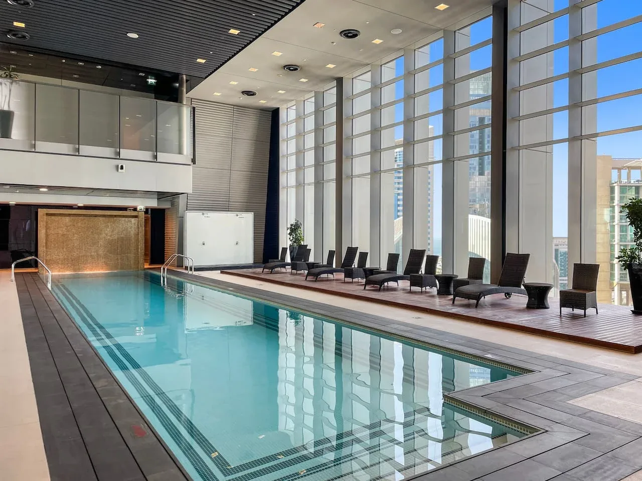 An indoor swimming pool with lounge seating beside tall windows.