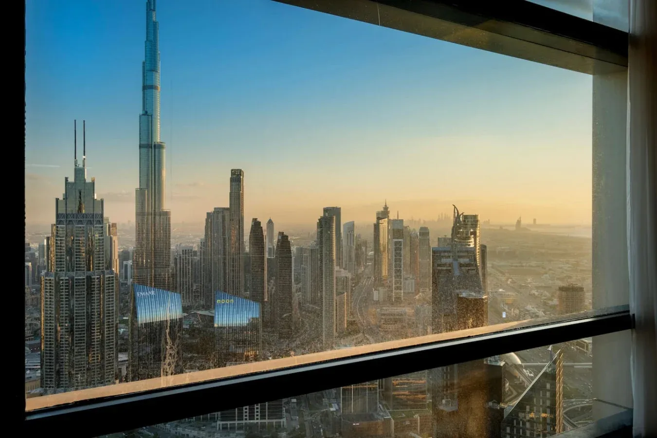 A city skyline viewed through a large window at sunset.