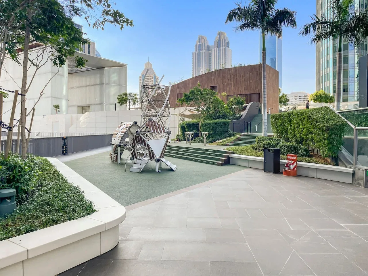 A landscaped outdoor plaza has paved walkways, raised planters, and sculptural seating.