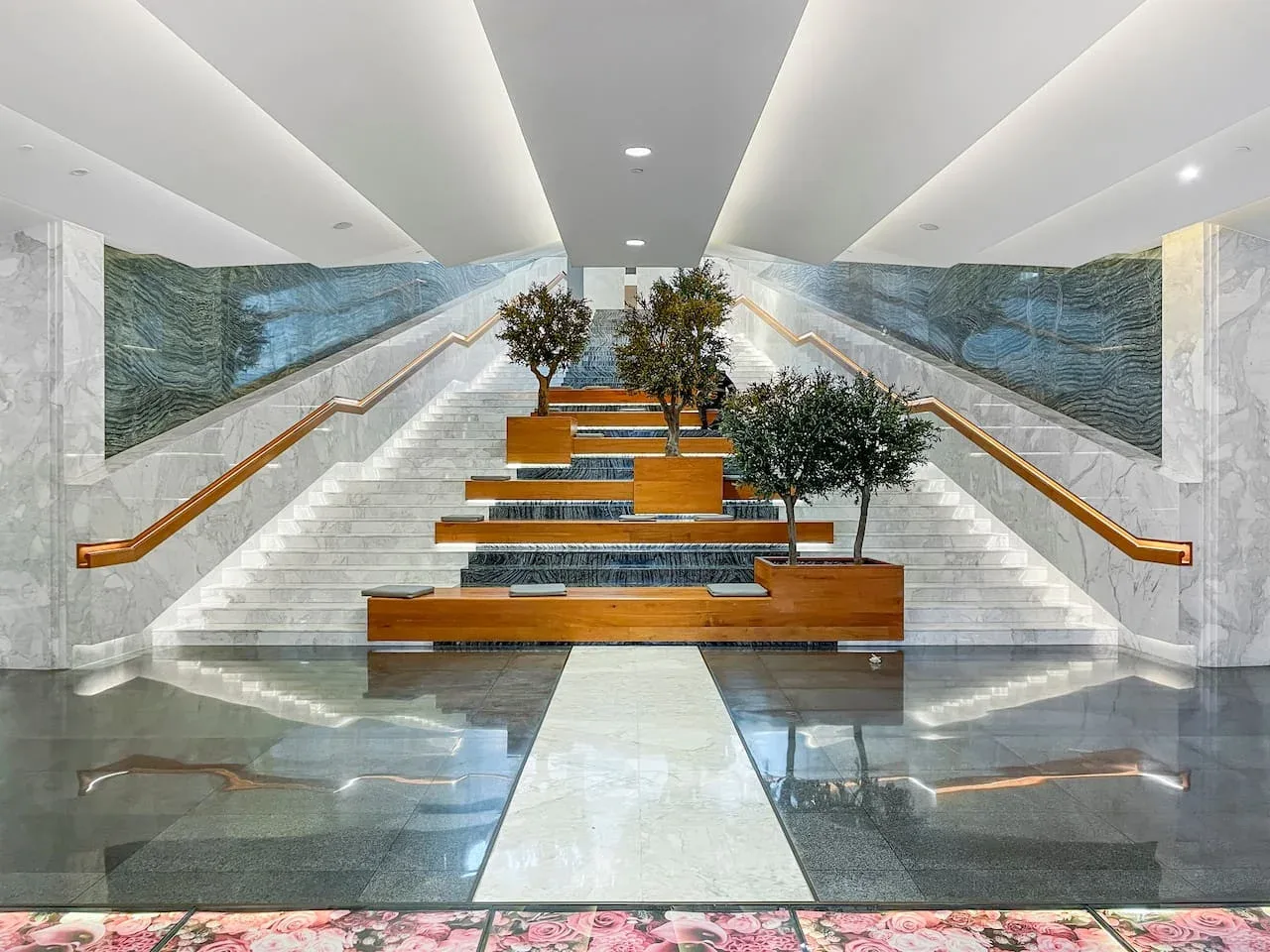 A broad marble staircase rises beneath a bright ceiling, with planters along the center.