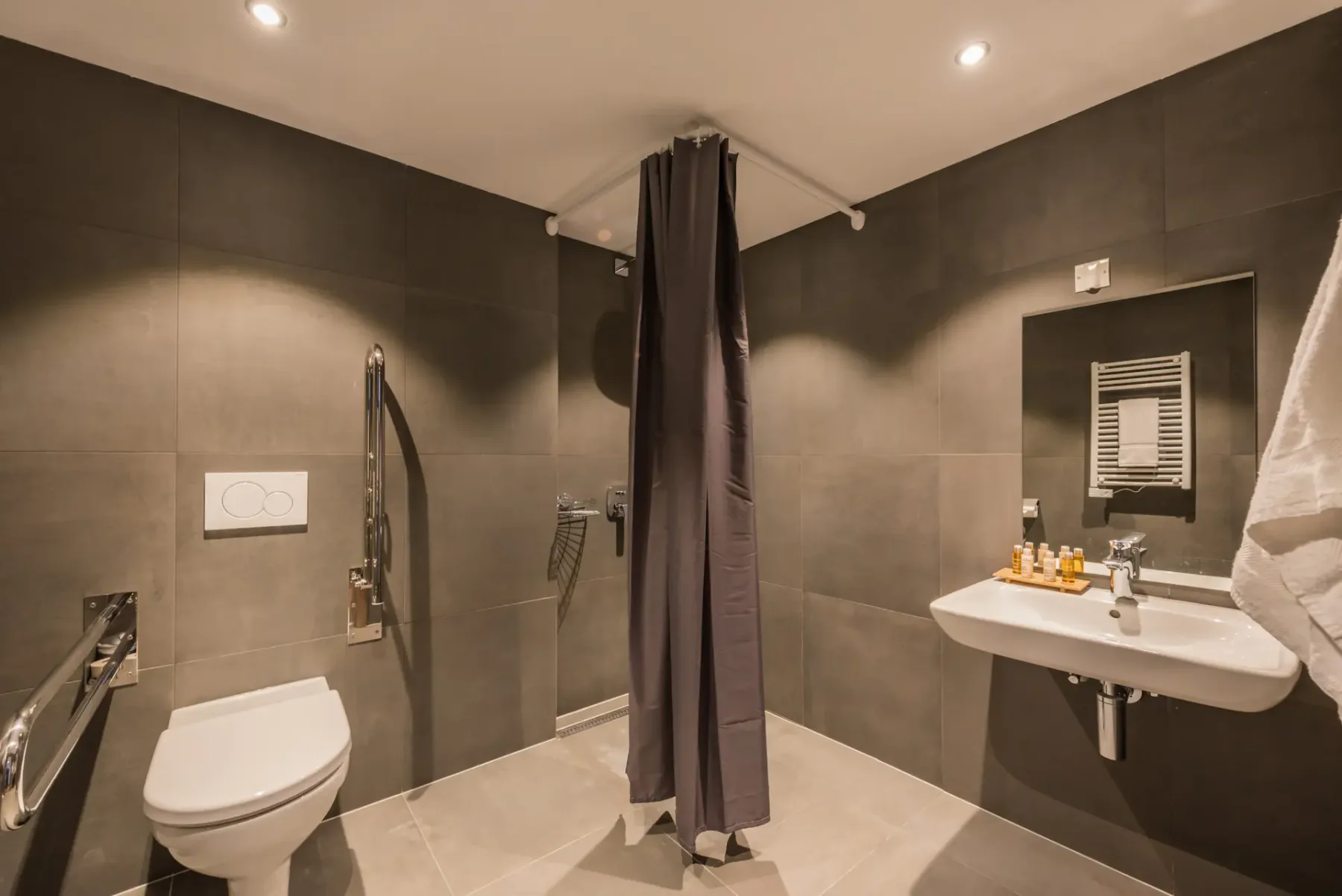 A tiled bathroom with a shower curtain, toilet, and wall-mounted sink.