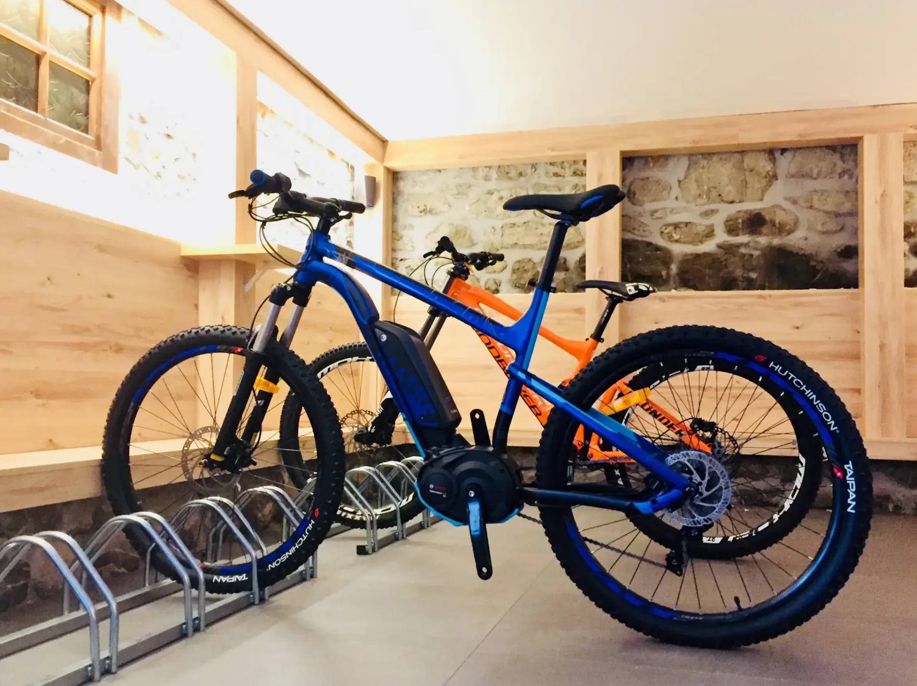 Mountain bikes are parked on racks in a bright room with stone walls.