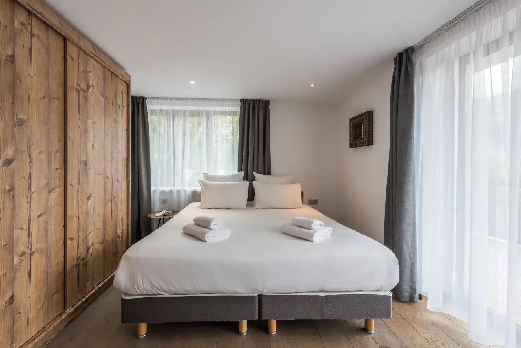 A bedroom with a bed, folded towels, and sheer curtains.