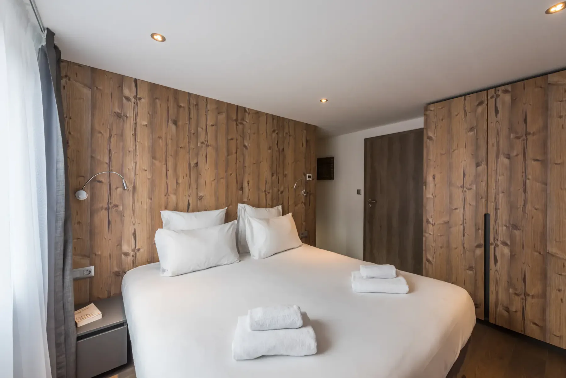 A bedroom with a double bed, white bedding, and wood-paneled walls.