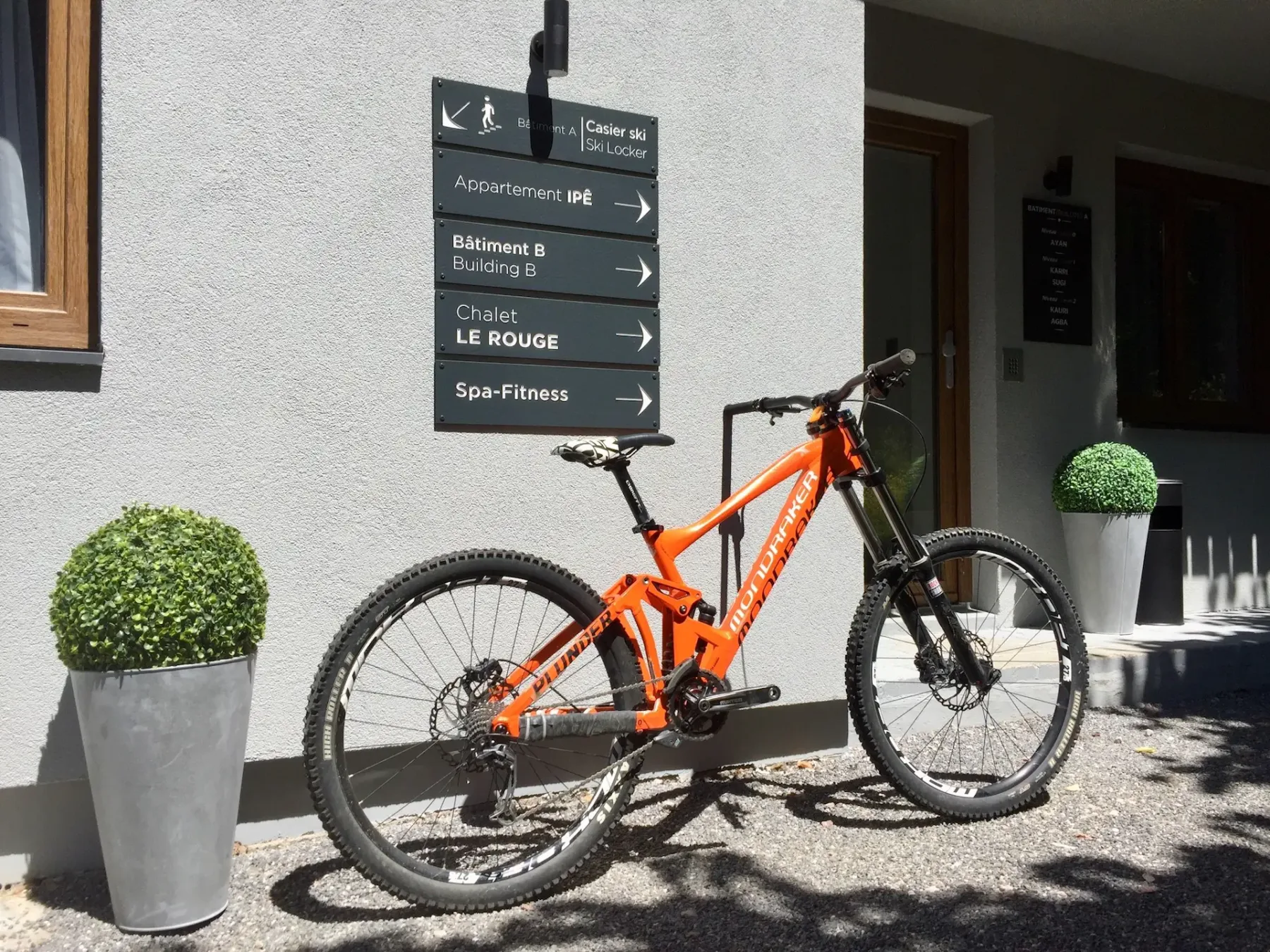 An orange mountain bike is parked beside a building entrance with directional signs.