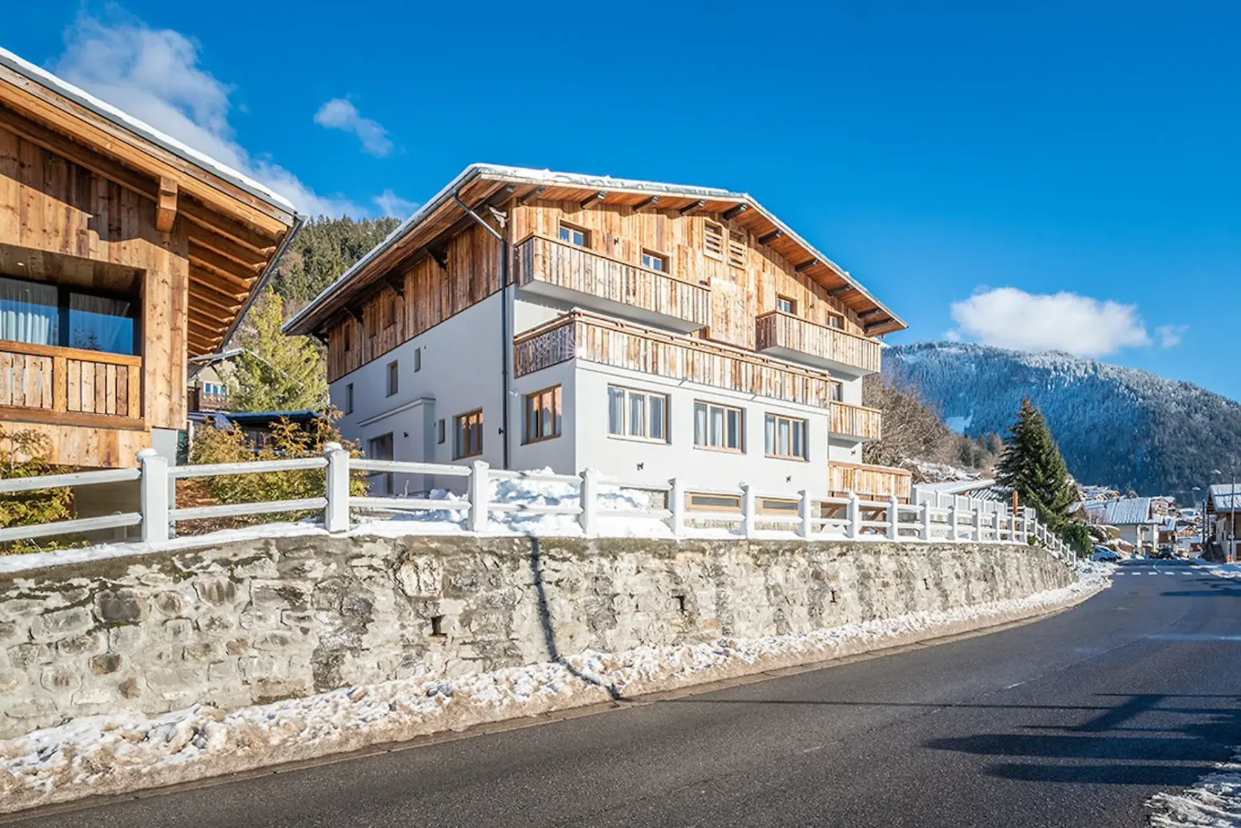 A chalet-style building stands beside a snowy roadside, with mountains in the background.