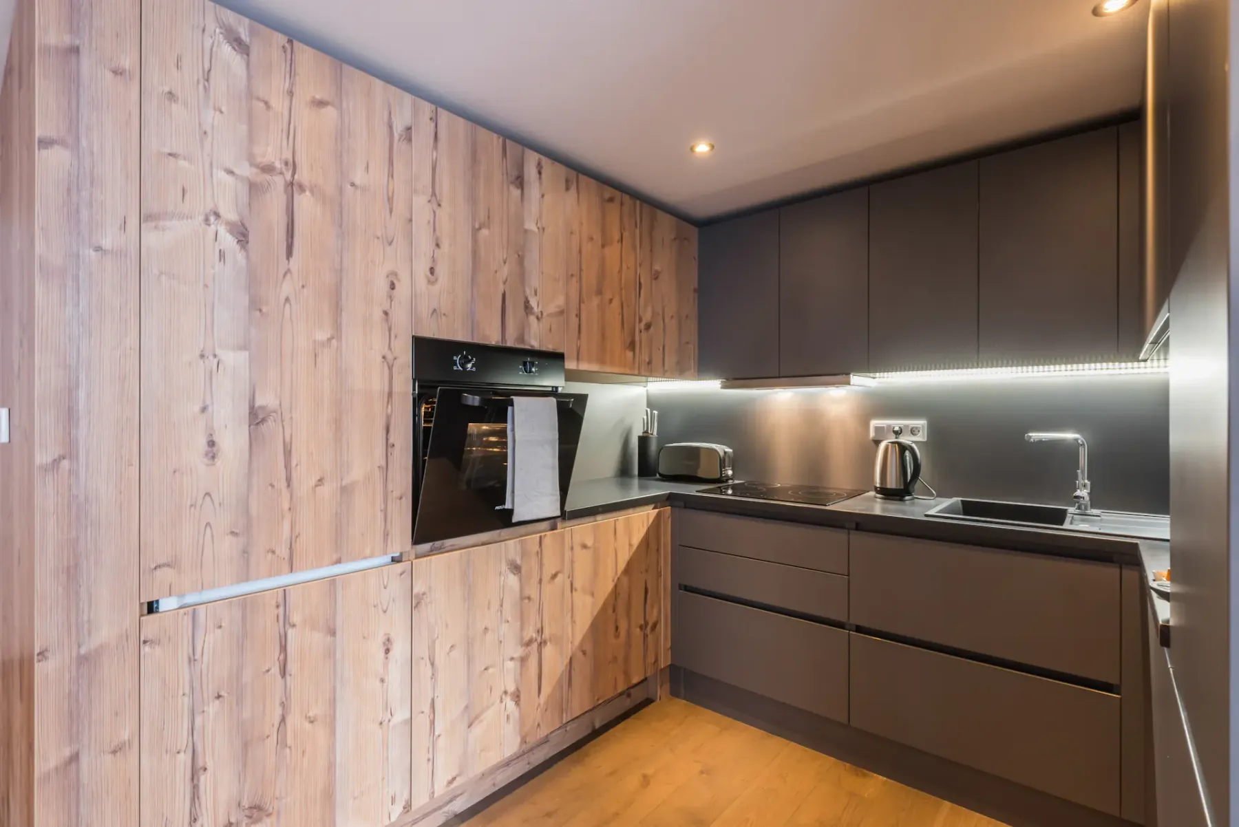 A modern kitchen with wood cabinetry, dark cabinets, and a built-in oven.