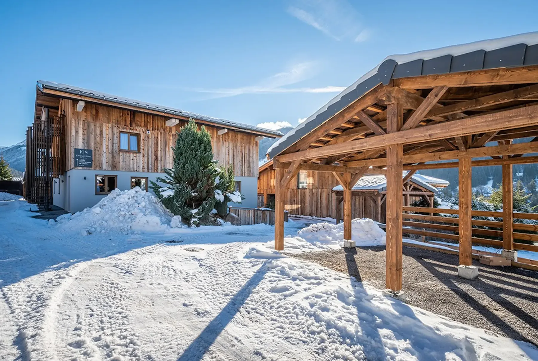 Snow-covered chalet exterior with a wooden covered parking area in the foreground.