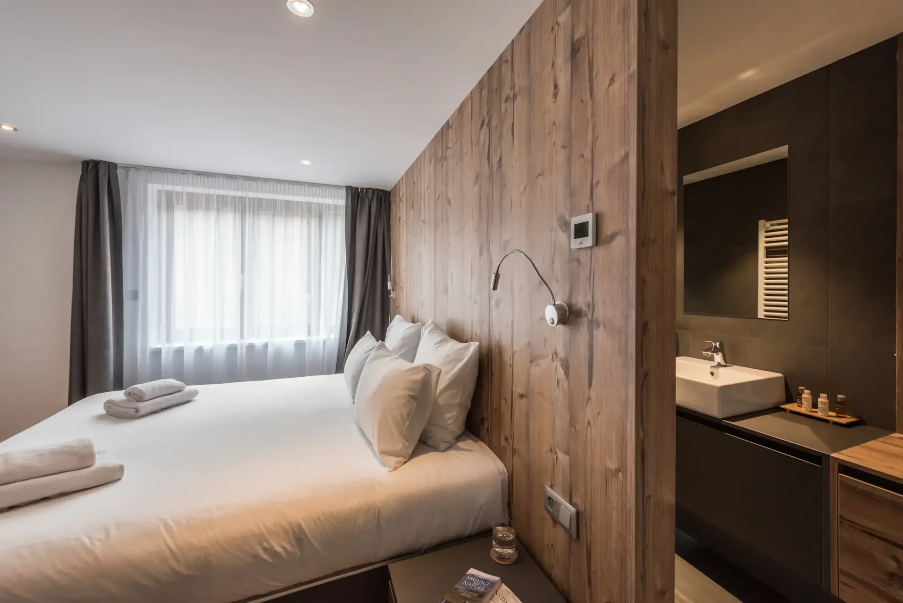 A bedroom with a neatly made bed beside a compact bathroom area.