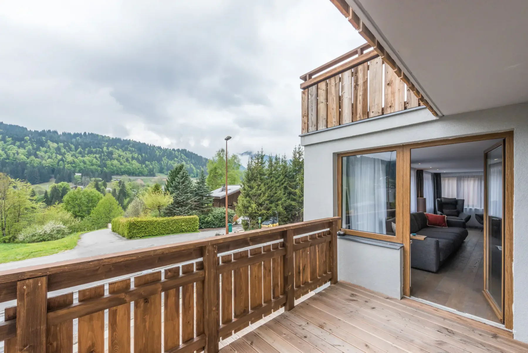A wooden balcony overlooks a green hillside, with an open doorway beside it.
