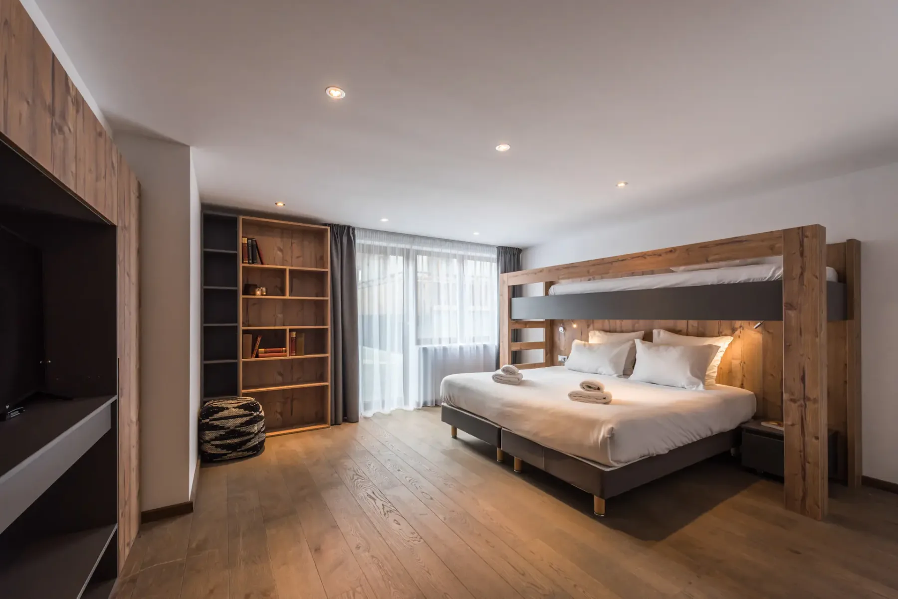 A bedroom with a large bed, wooden shelving, and a curtained window.