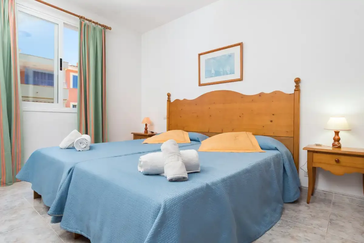 A bedroom with blue bedding, wooden headboard, and a window with green curtains.