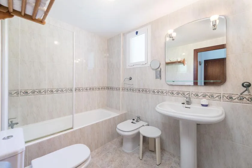 A tiled bathroom with a bathtub, toilet, and sink beneath a wall mirror.