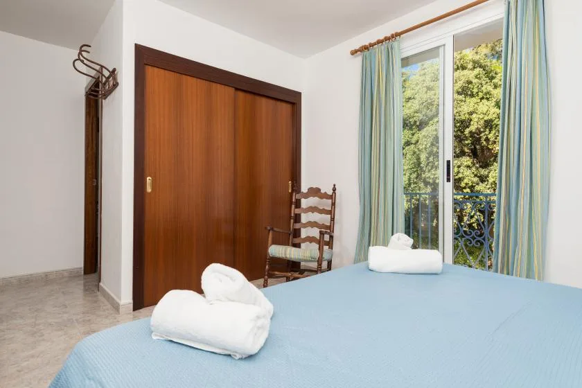 A bedroom with a blue bed, wooden wardrobe, and a glass door opening to greenery.