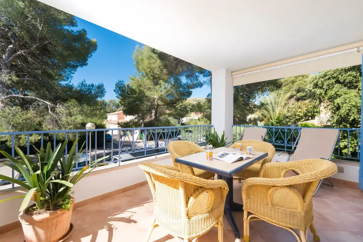 A covered outdoor dining area with wicker seating overlooks leafy trees.