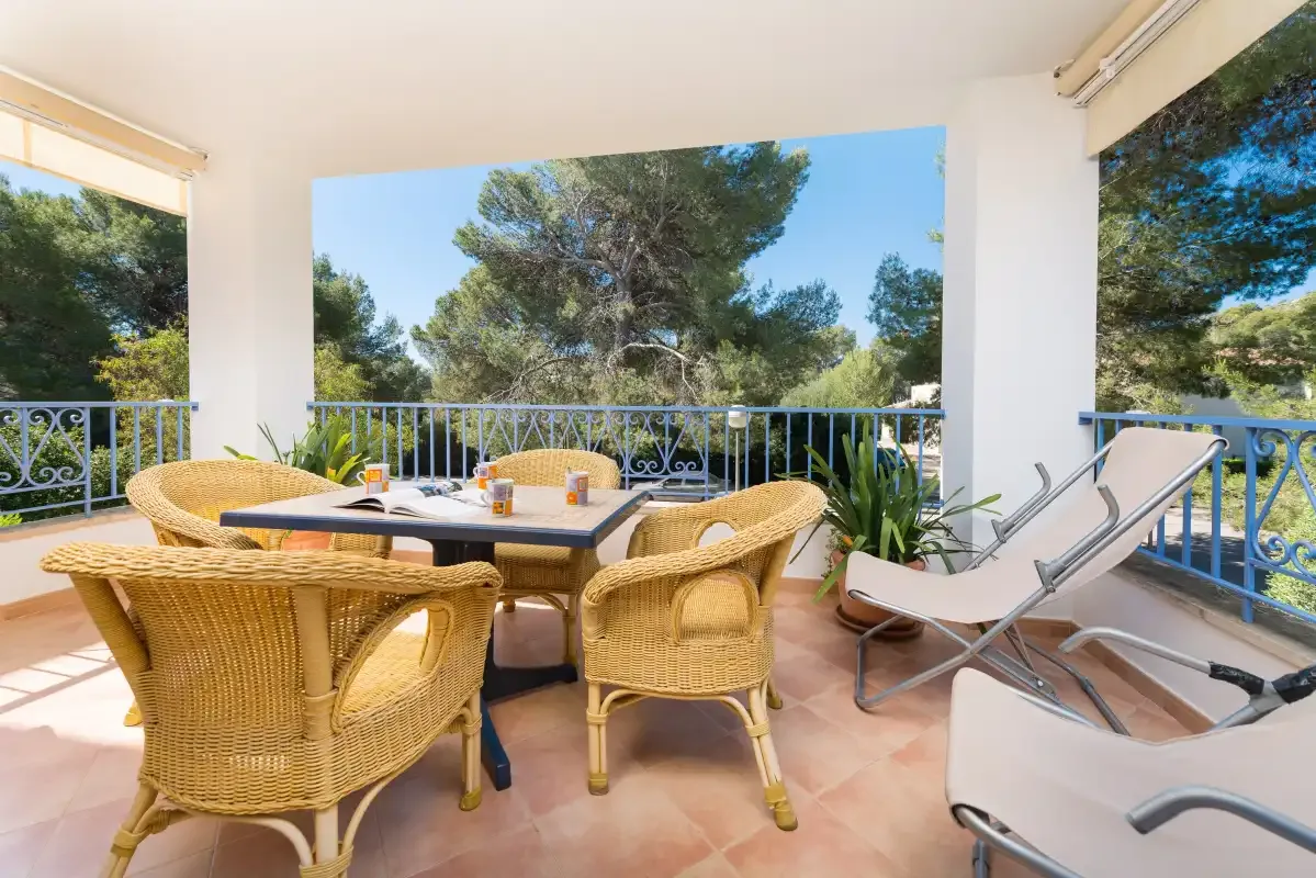 A covered terrace with wicker seating, a dining table, and views of trees.