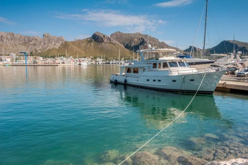 A white boat is moored in a marina with rocky mountains in the background.