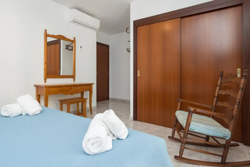 Bedroom with a bed, wooden wardrobe, and a chair beside a dressing table.