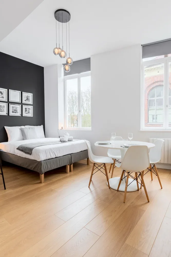 A bright bedroom with a bed, a small dining table, and large windows.