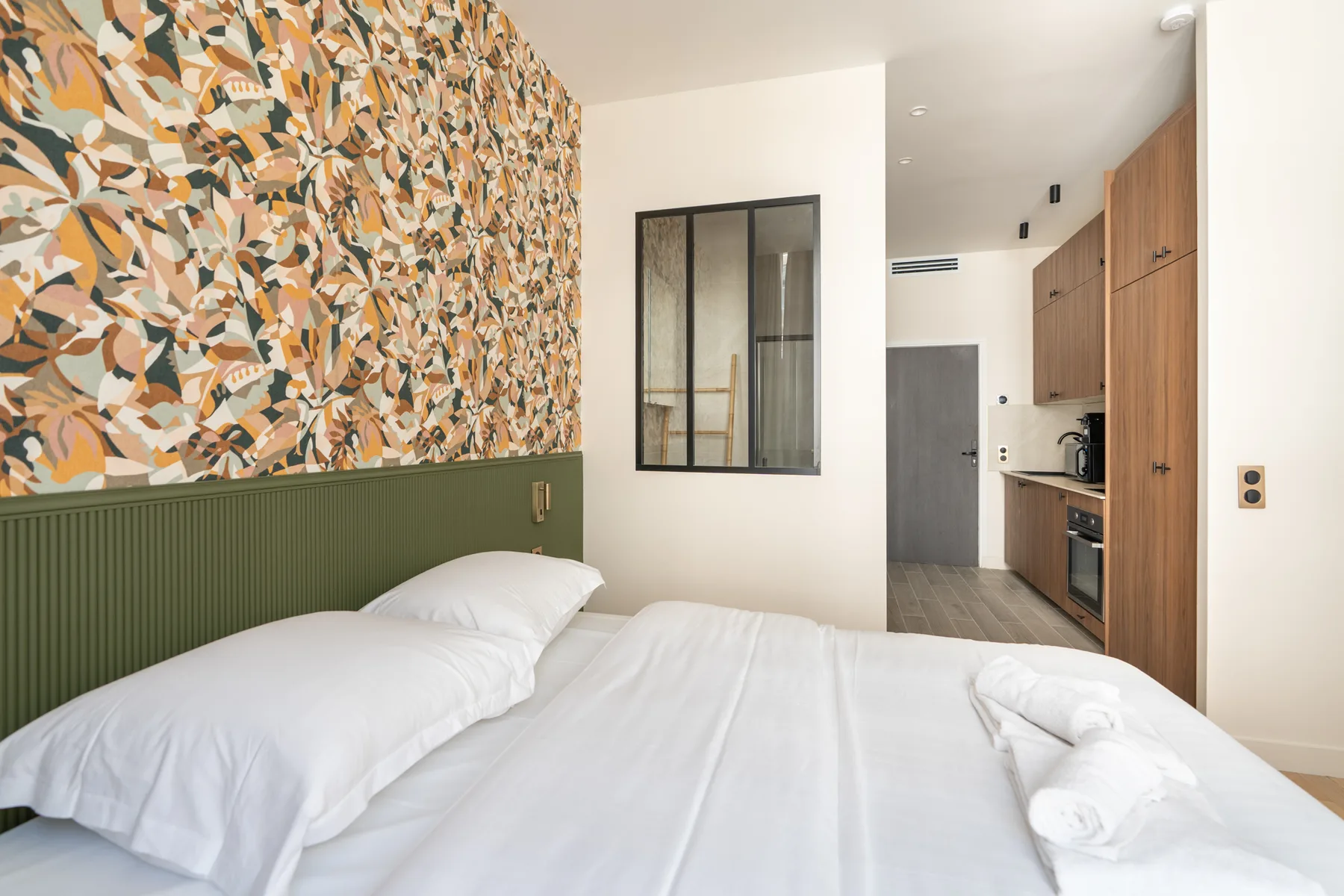 Dormitorio con ropa de cama blanca y una pequeña zona de cocina.