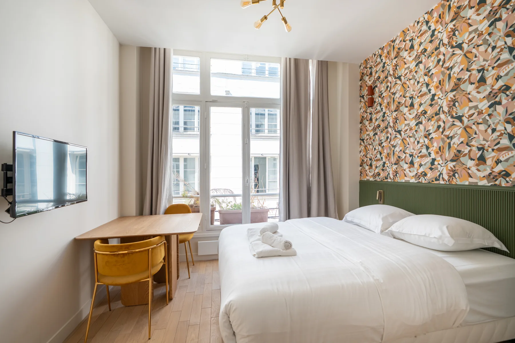 A bright bedroom with a large bed, desk, and tall windows.