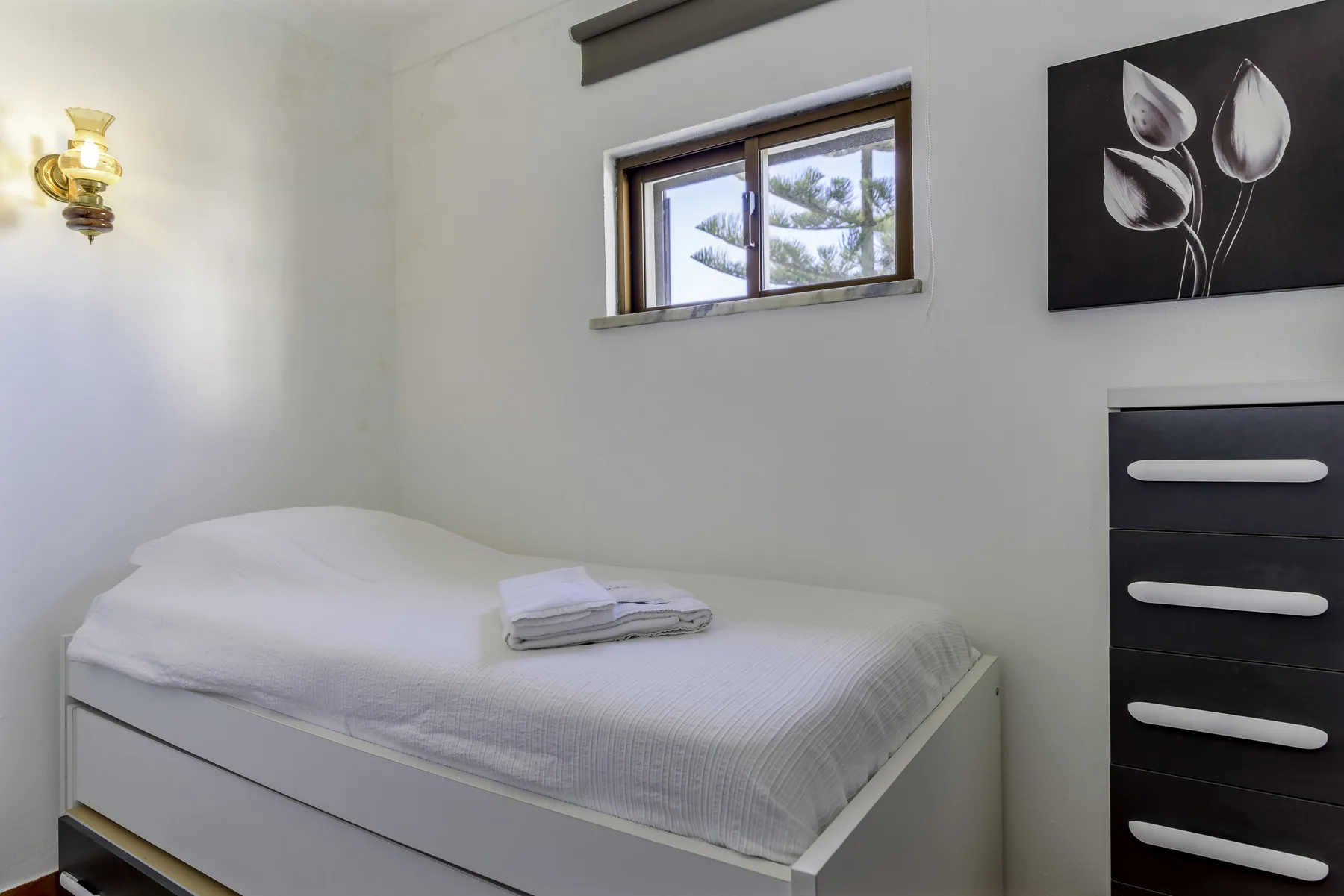 Un dormitorio luminoso con una cama bien hecha bajo una ventana pequeña.