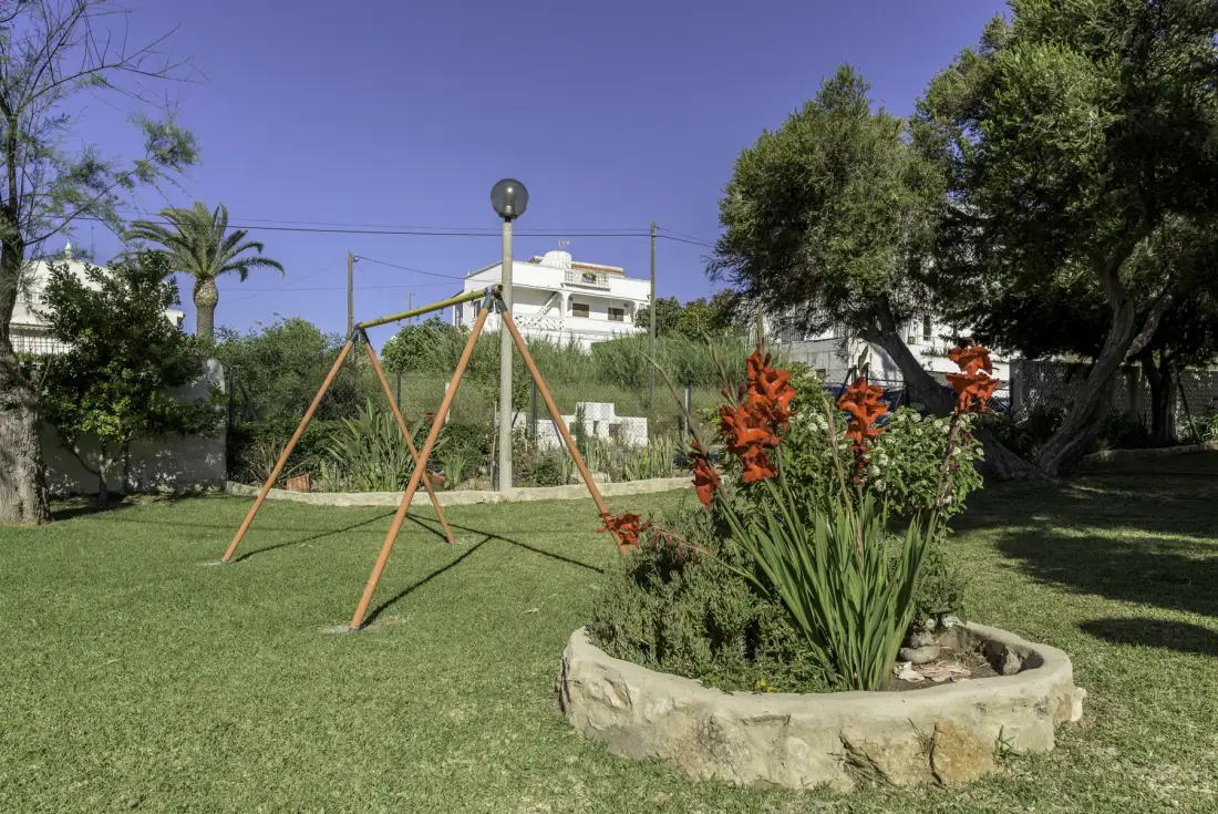 Un jardín con césped, un columpio y un arriate circular.