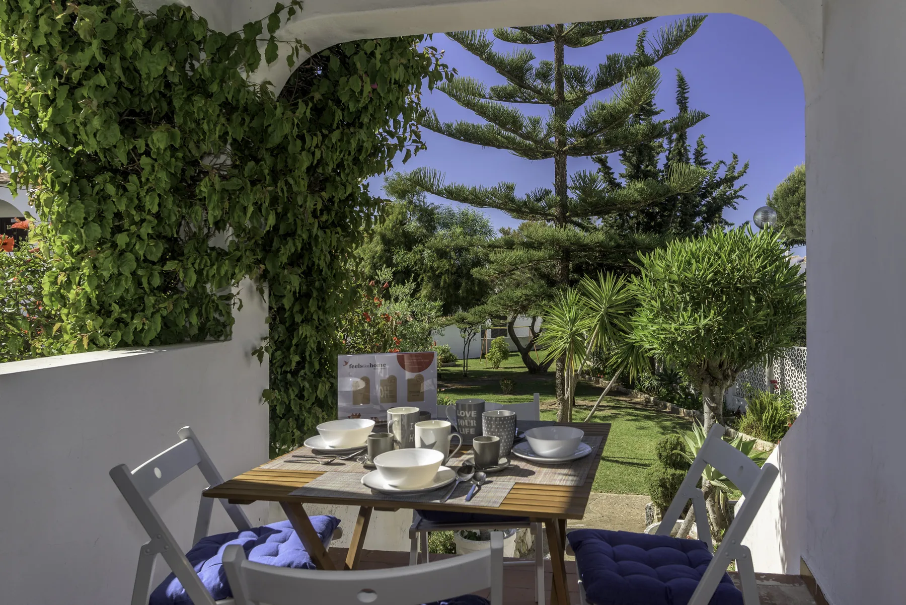 Una zona de comedor exterior a la sombra da a un jardín verde.