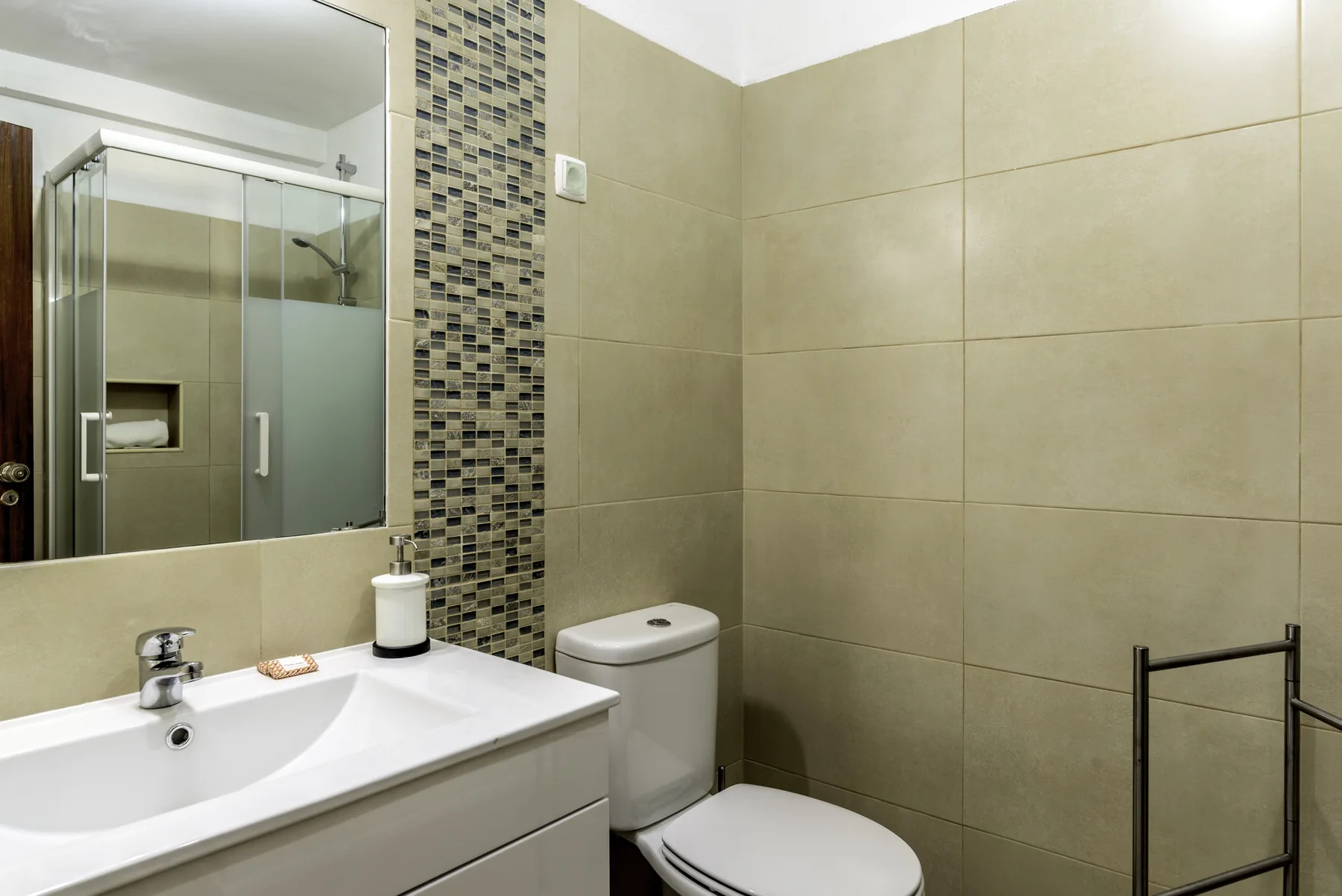 Un baño alicatado con lavabo, espejo e inodoro.