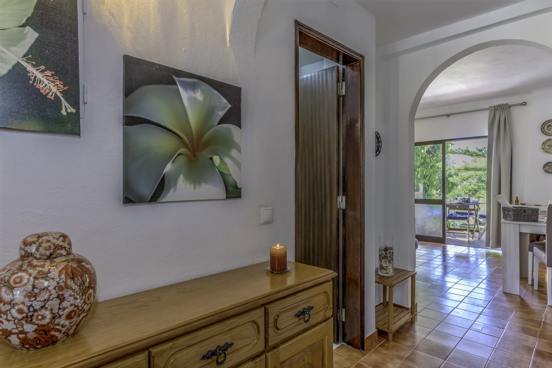 Un pasillo interior se abre bajo un arco a un comedor luminoso con vistas al jardín.