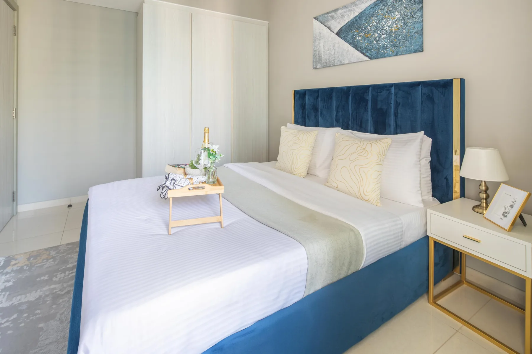 Un dormitorio luminoso con una cama de ropa blanca y cabecero tapizado azul.