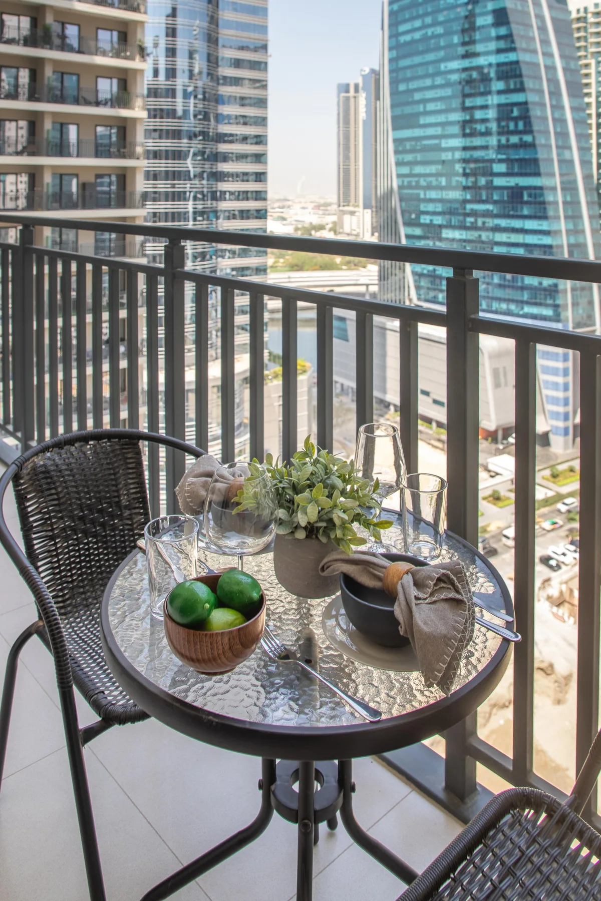 Una pequeña zona de estar en un balcón con una mesa de vidrio y edificios altos a la vista.