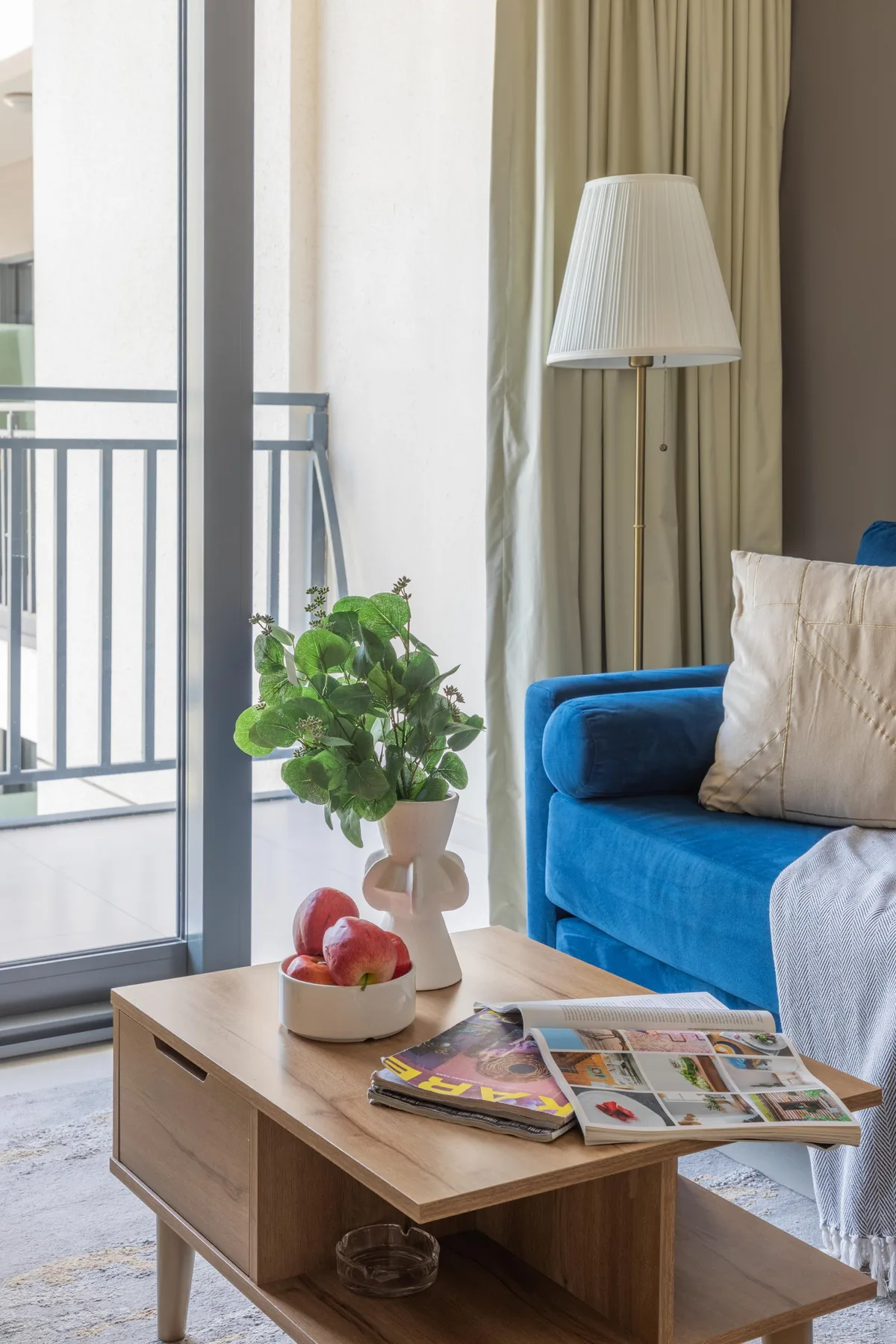 Una sala de estar con asientos azules, una mesa de centro de madera y una lámpara de pie junto a la ventana.
