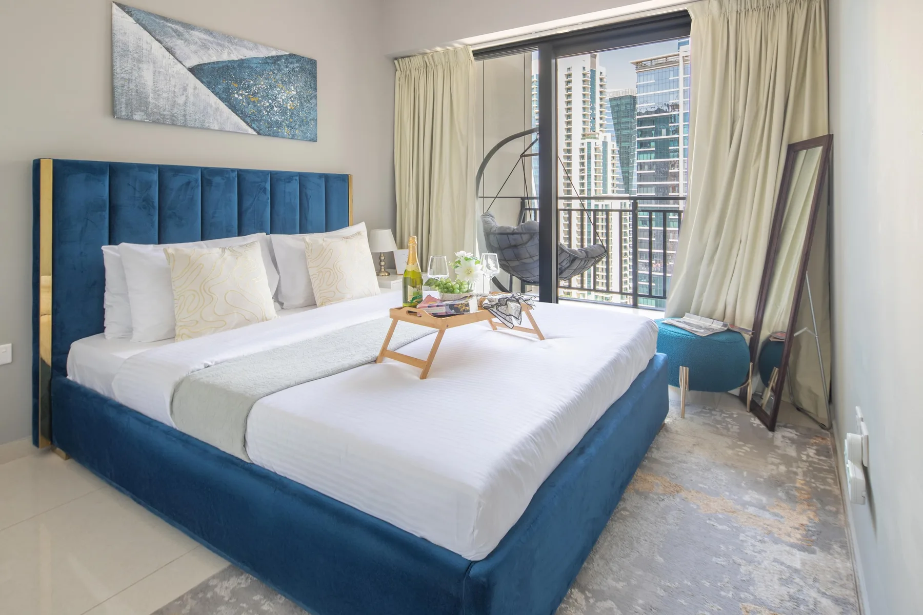Un dormitorio con una cama tapizada azul y ventanales con vistas a edificios de la ciudad.