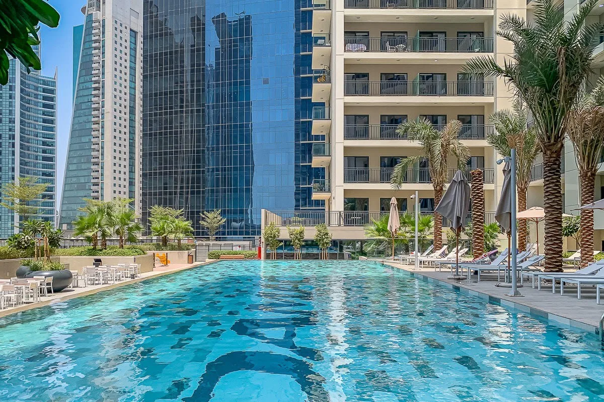 Una piscina al aire libre está rodeada de palmeras y edificios altos.