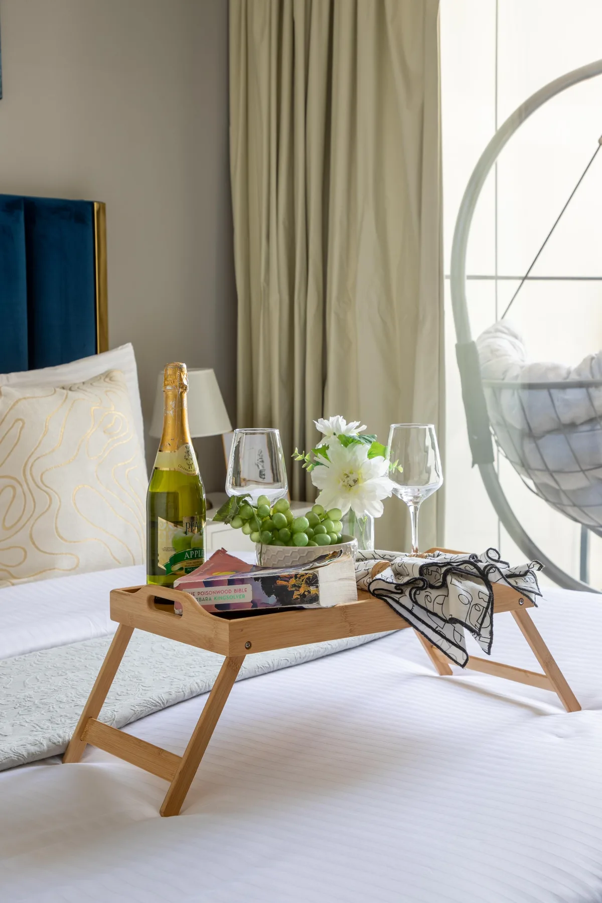 Un dormitorio con una cama, una bandeja de desayuno y una silla colgante junto a la ventana.
