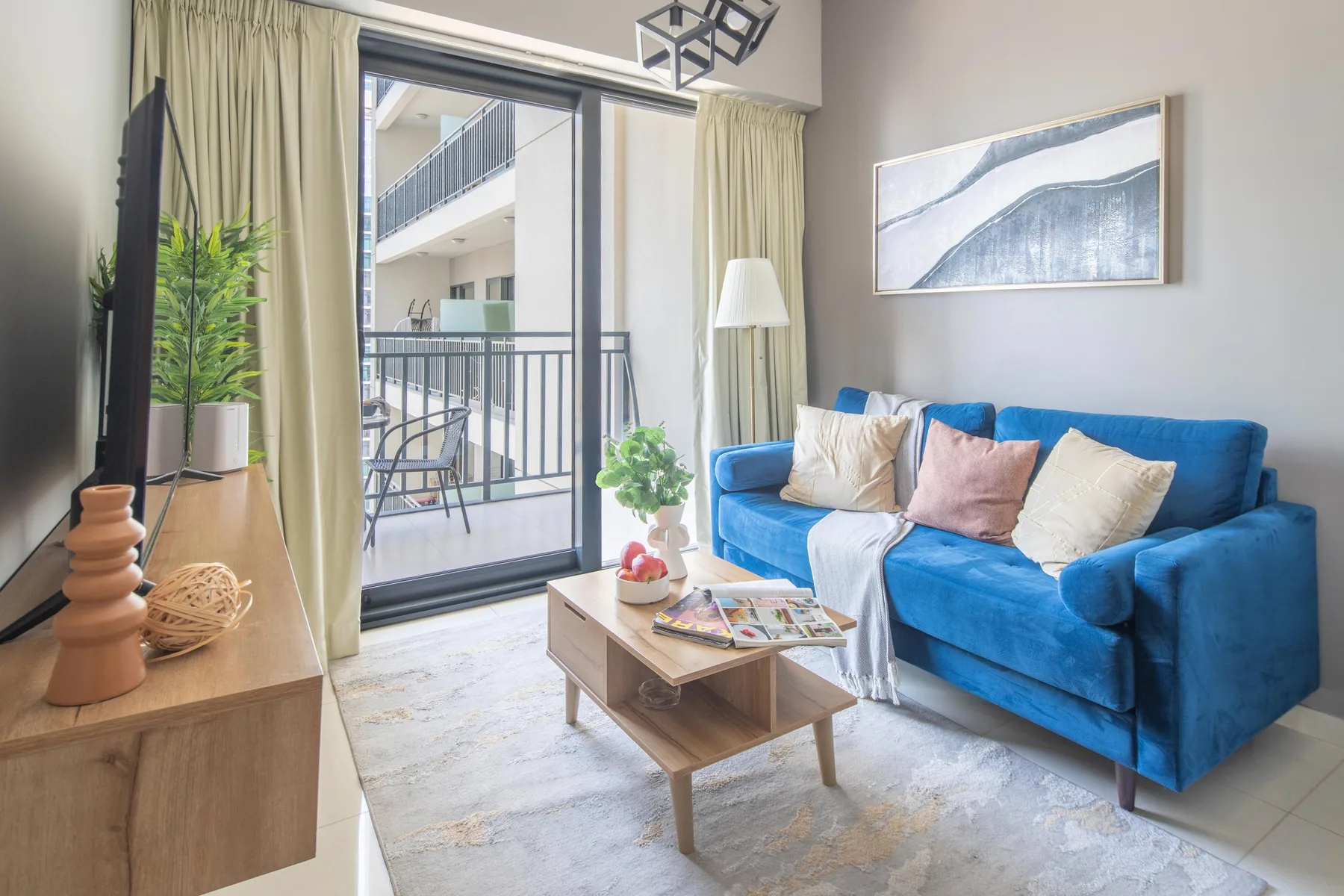 Sala de estar con un sofá azul junto a una puerta de vidrio al balcón.