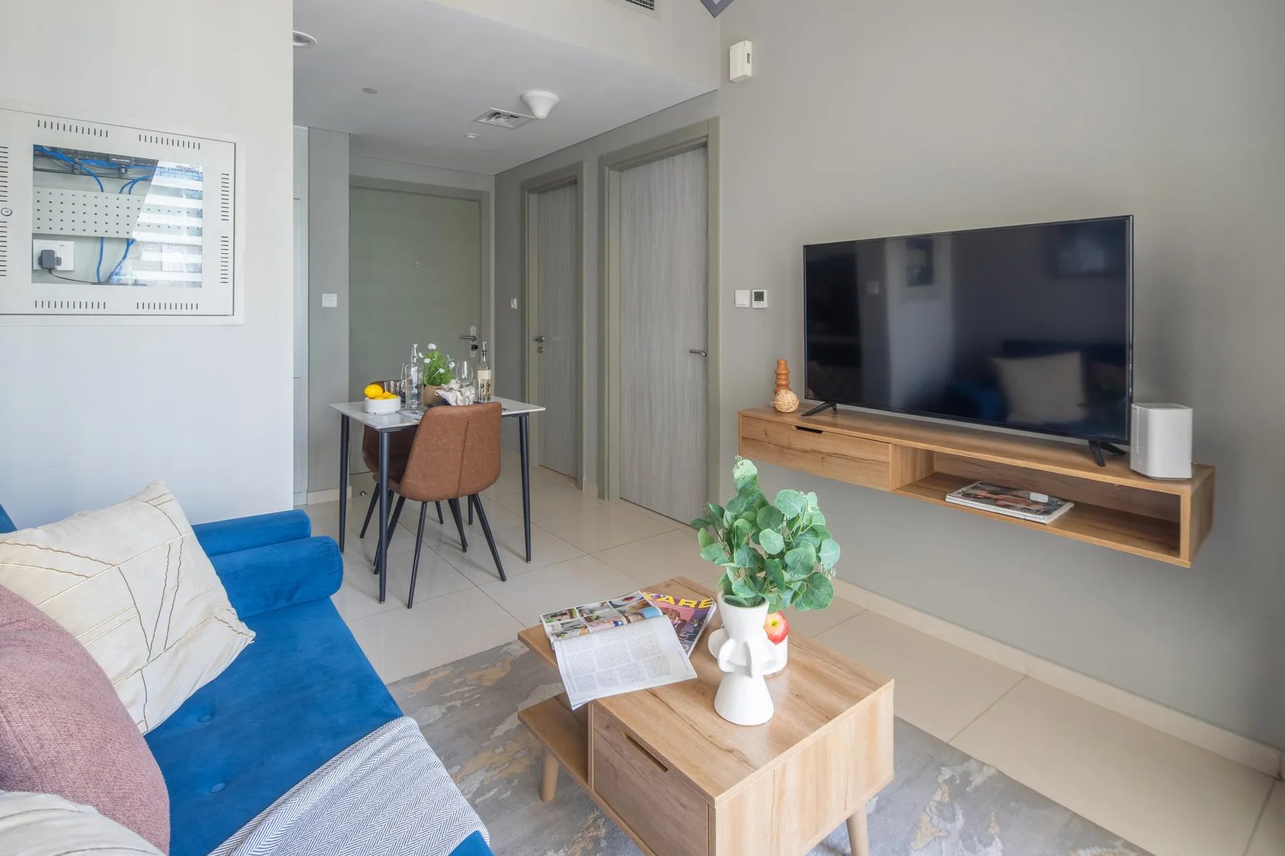 Una sala de estar con asientos azules, una mesa de centro y un televisor en la pared.