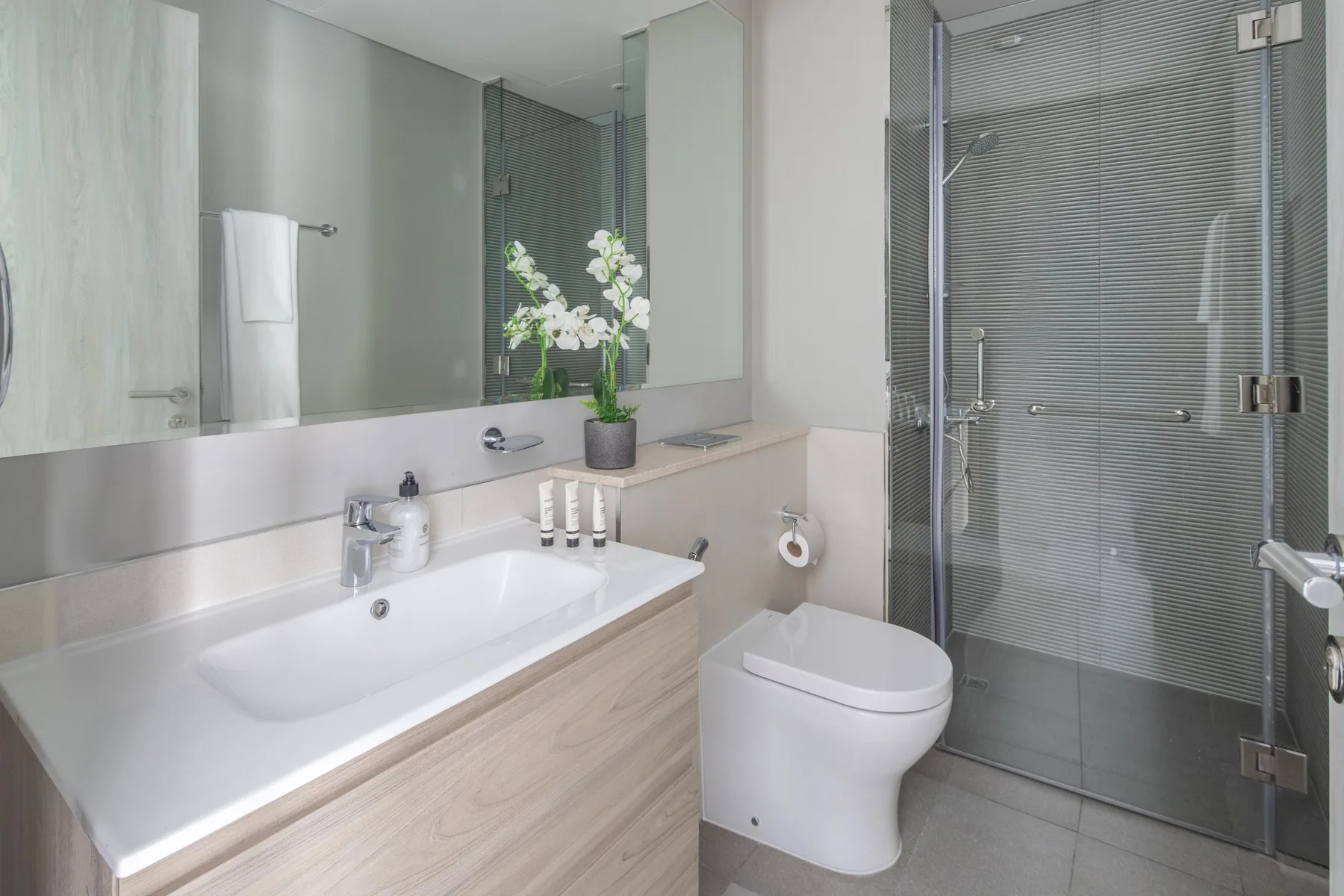 Un baño moderno con lavabo, inodoro y ducha con mampara de vidrio.