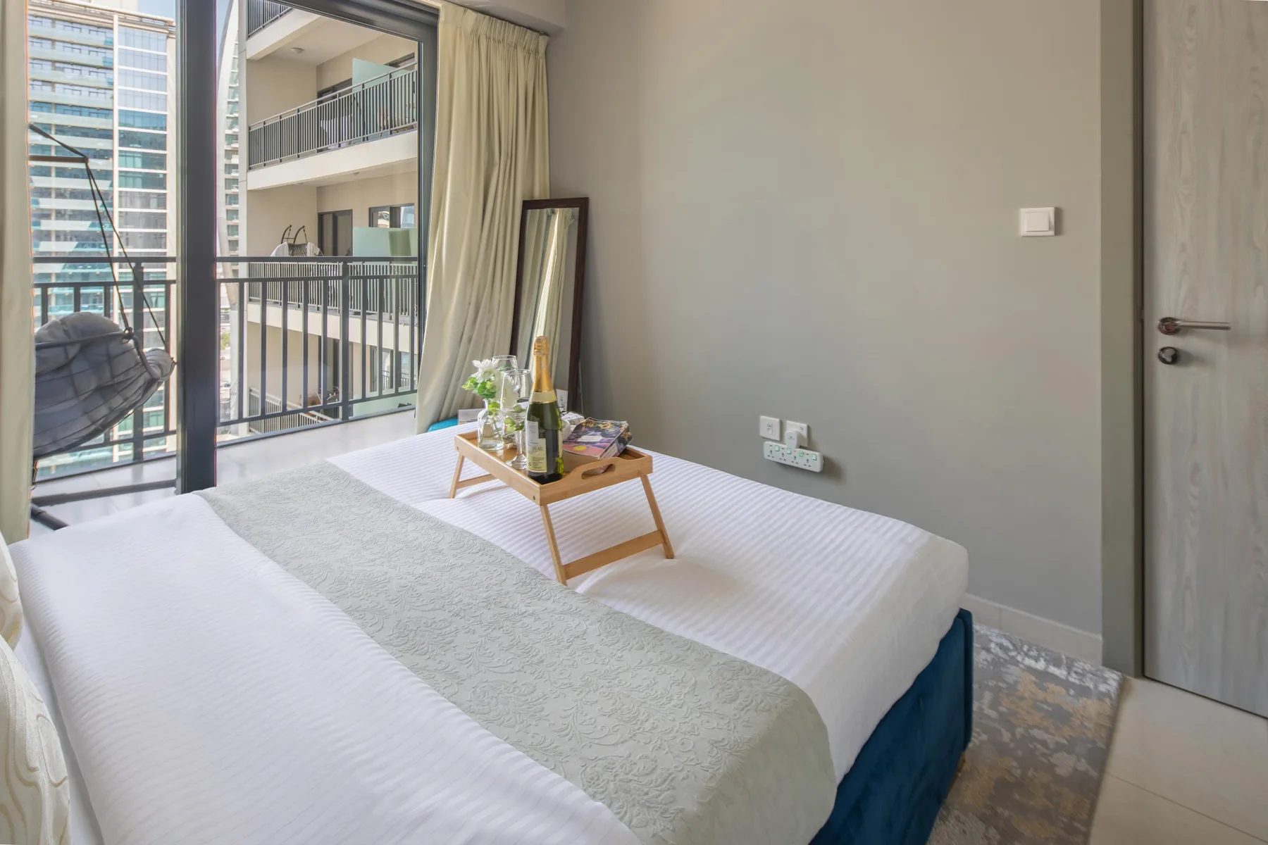 Un dormitorio con una cama bien hecha y una mesita junto a las puertas del balcón.