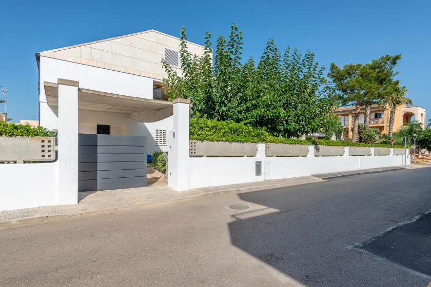 Un edificio blanco moderno se alza tras un muro bajo junto a una calle pavimentada.