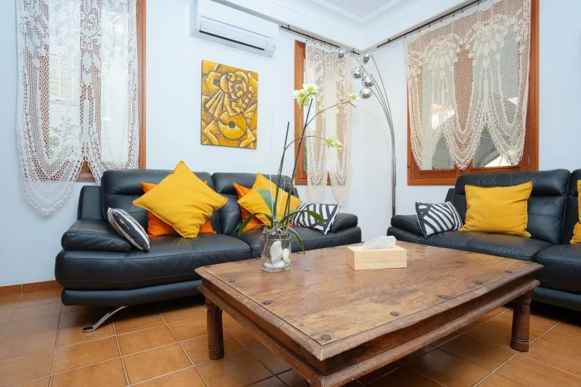 Una sala de estar con asientos oscuros, cojines coloridos y una mesa de centro de madera.