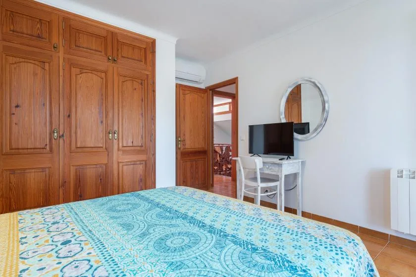 Un dormitorio con una colcha estampada, armarios de madera y un pequeño escritorio.